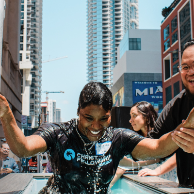 Smiling woman emerging from baptism tank during Christ Fellowship downtown Miami street baptism with towers in background.